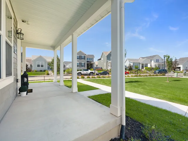 Covered front porch with concrete flooring, supported by multiple white pillars, featuring a wall-mounted light fixture