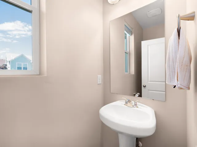 Pedestal sink with chrome fixtures, rectangular wall-mounted mirror, and a window with white trim