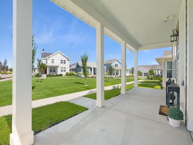 Covered front porch with white columns, concrete flooring, and a beadboard ceiling