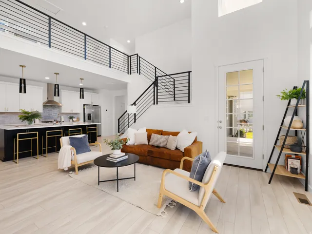 Open-concept living space featuring high ceilings, wood-finish flooring, a contemporary kitchen with an island, and a second-story interior balcony with black railing