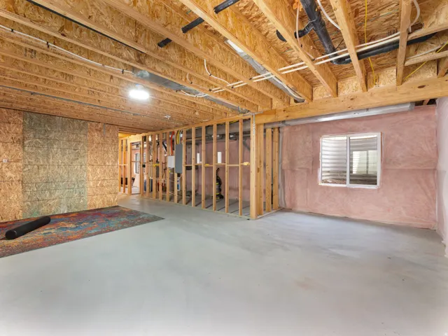 Unfinished basement with exposed ceiling joists, framed interior walls, visible insulation, and a single window