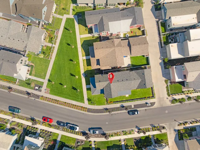 Aerial perspective showcasing a residential area with manicured green spaces, paved streets, and a variety of detached homes with gray shingle roofs