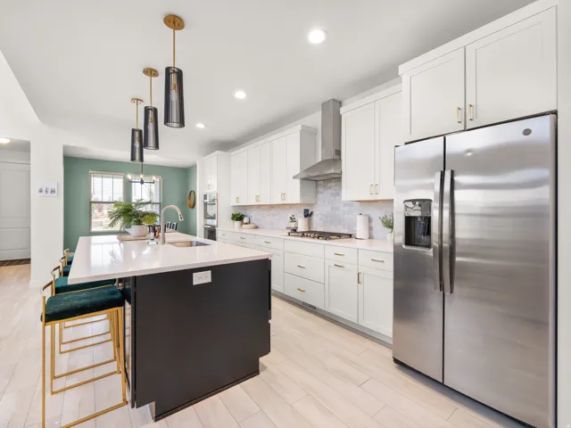 Kitchen featuring a large island with sink, stainless steel appliances, white cabinetry, and wood-finish flooring