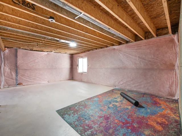 Unfinished basement featuring exposed wood joists, concrete flooring, and insulated walls