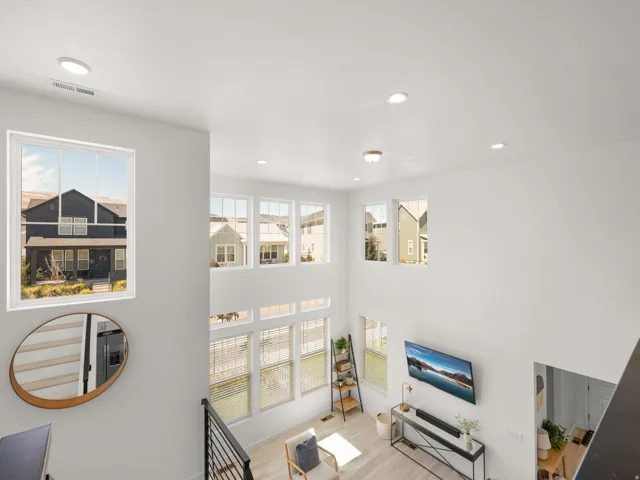 Two-story ceiling, multiple large windows, recessed lighting, light wood-finish flooring, and black metal railing