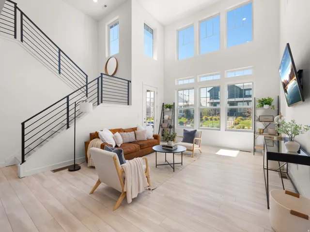 Two-story living area with light wood-finish flooring, a contemporary staircase featuring black horizontal railings, and a wall of windows