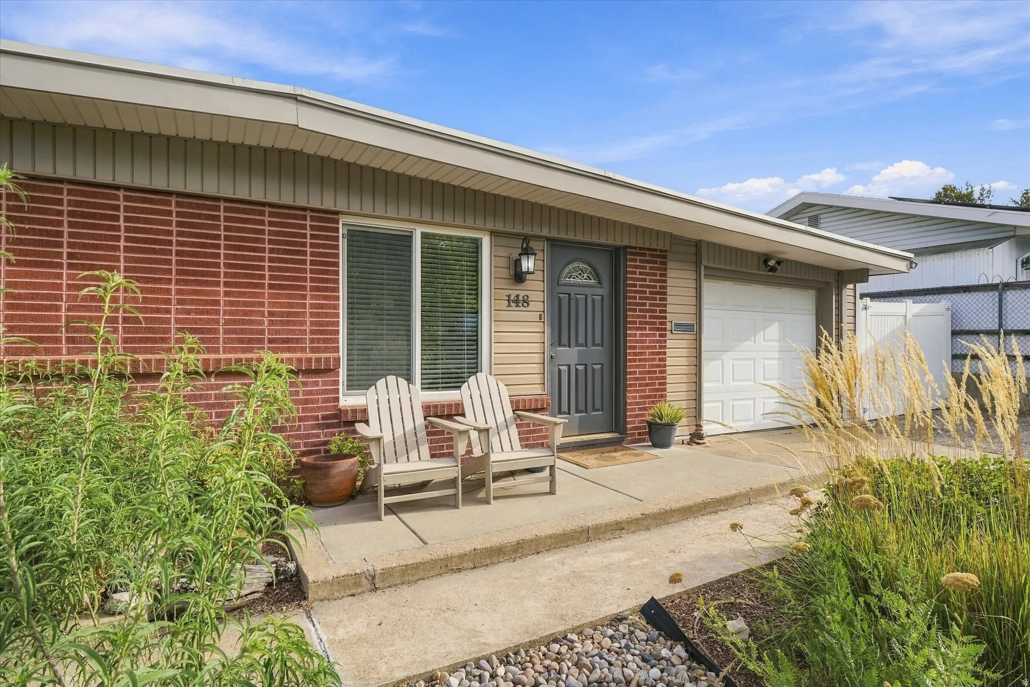 Brick and siding exterior with a single-panel garage door, concrete pathway, and mature landscaping