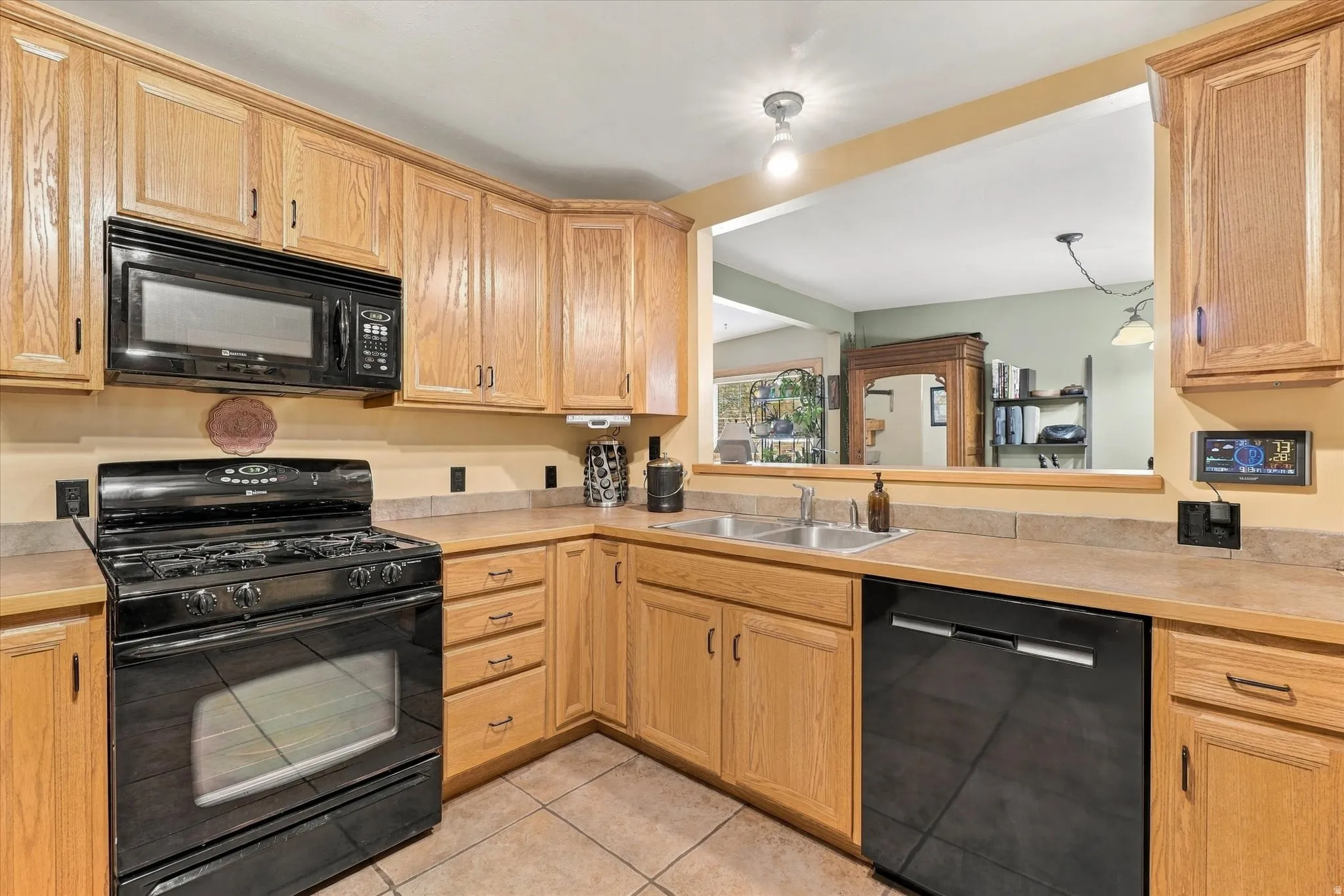 Kitchen featuring wood cabinetry, laminate countertops, a double basin stainless steel sink, tile flooring, and a pass-through window