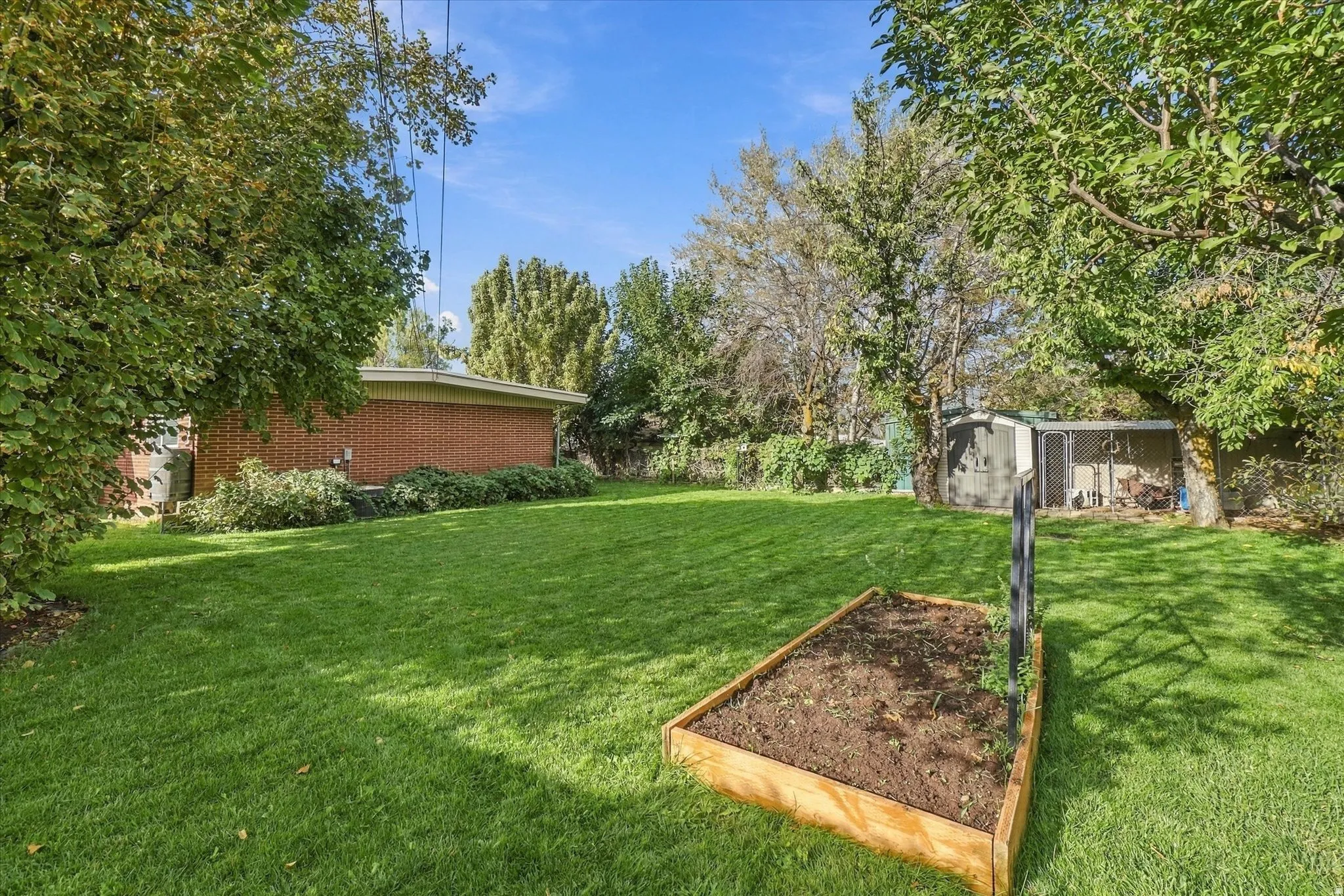 Expansive lawn with mature trees, a raised garden bed, and a brick-sided structure