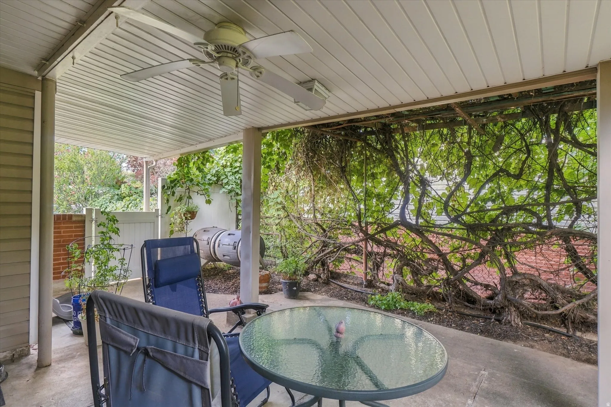 Covered patio with a ceiling fan, concrete flooring, and a trellis featuring extensive foliage