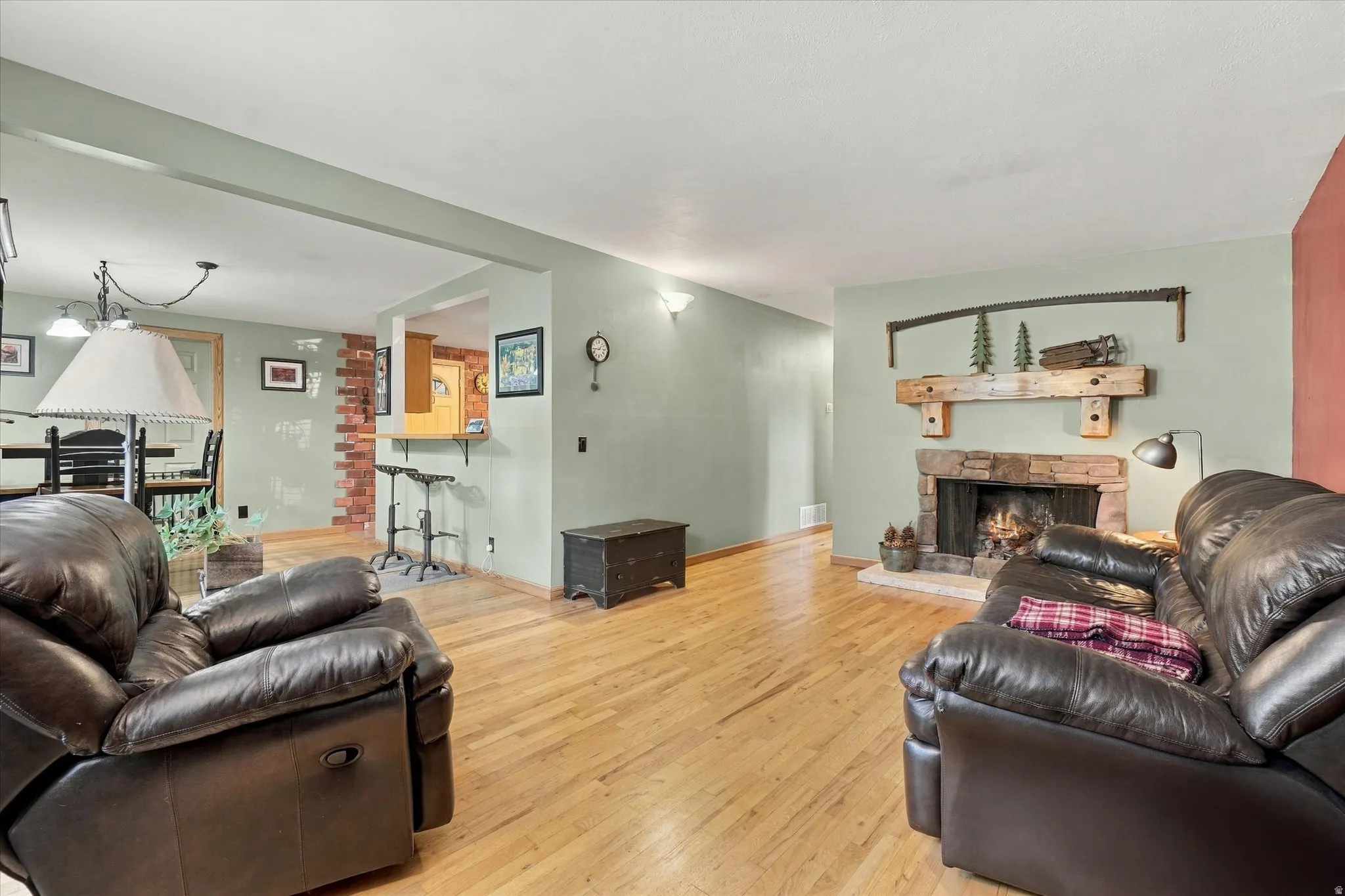 Wood-finish flooring throughout, stone-clad fireplace with wood mantel, exposed brick accent wall, and recessed lighting