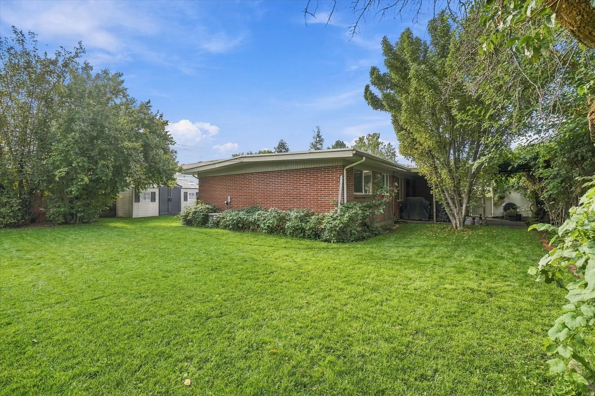 Expansive lawn area with mature trees, brick exterior, and a detached storage shed