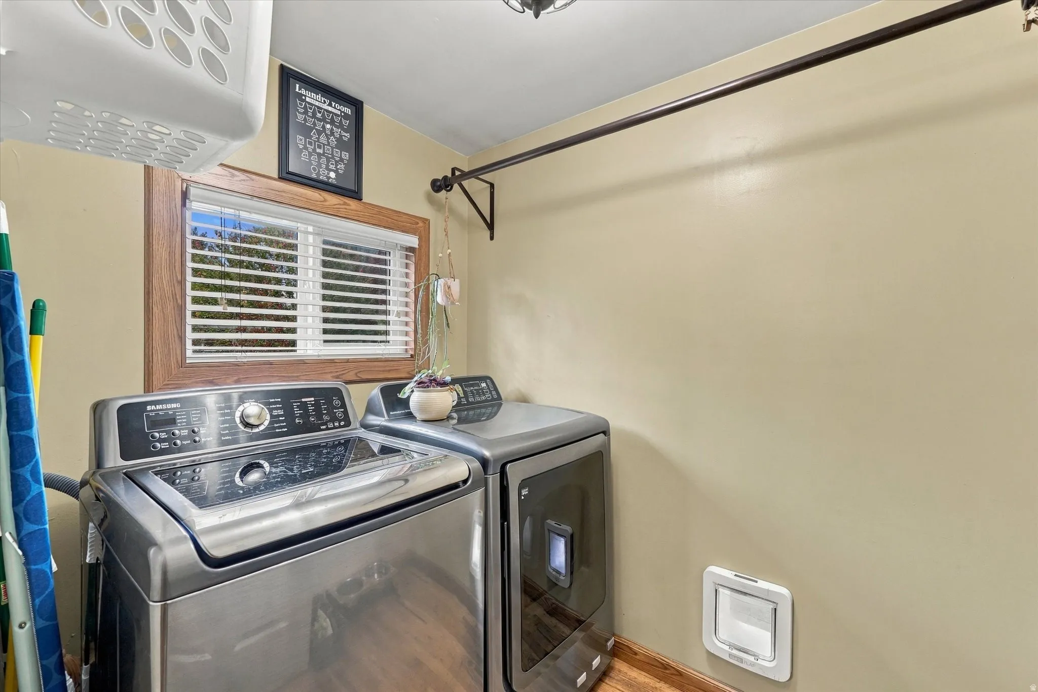Laundry area with wood-finish flooring, a wood-trimmed window, and wall-mounted drying rod