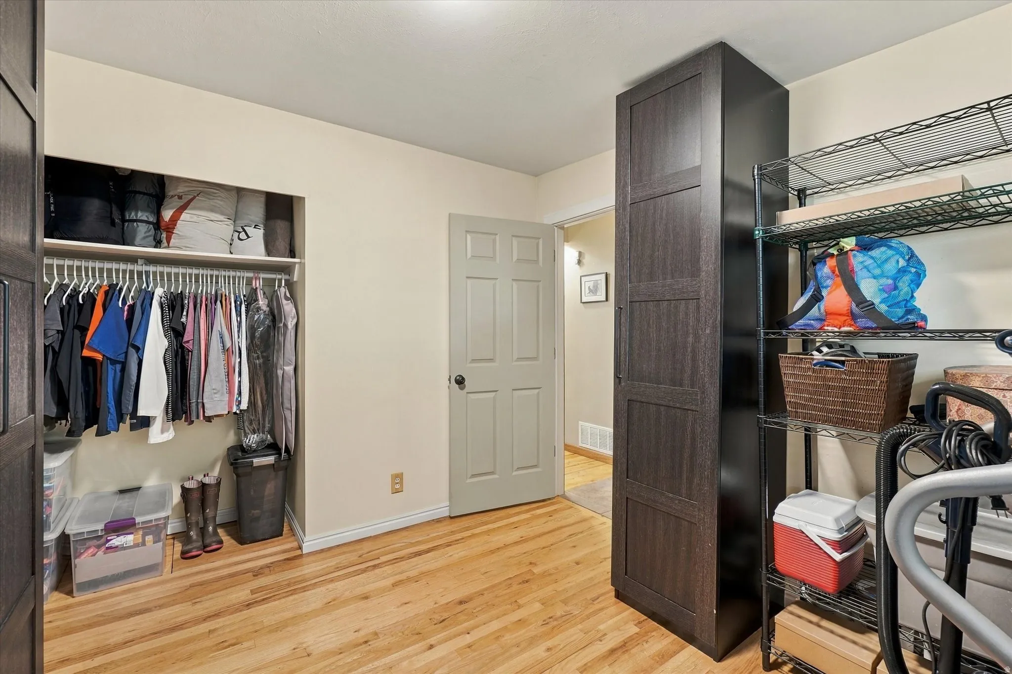 Wood-finish flooring, built-in open closet with shelving and hanging rod, tall dark wood-finish storage cabinet, and wire shelving unit