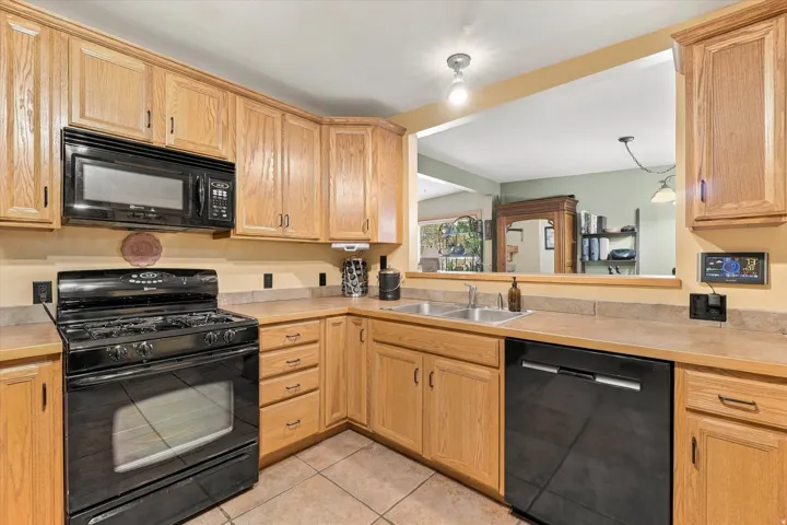 Kitchen featuring wood cabinetry, laminate countertops, a double basin stainless steel sink, tile flooring, and a pass-through window