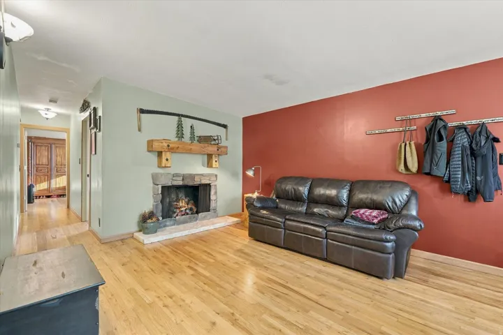 Stone-faced fireplace with a substantial wood mantel, natural wood flooring throughout, and recessed ceiling lighting