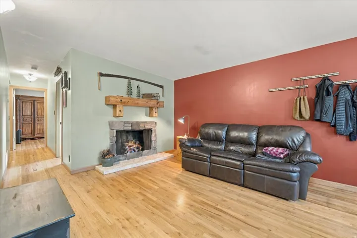Hardwood flooring throughout, stone-clad fireplace with a wood mantel, and contrasting wall colors