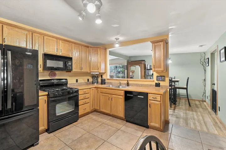 Kitchen featuring wood-finish cabinetry, tile flooring, black appliances, and a pass-through window to an adjacent room