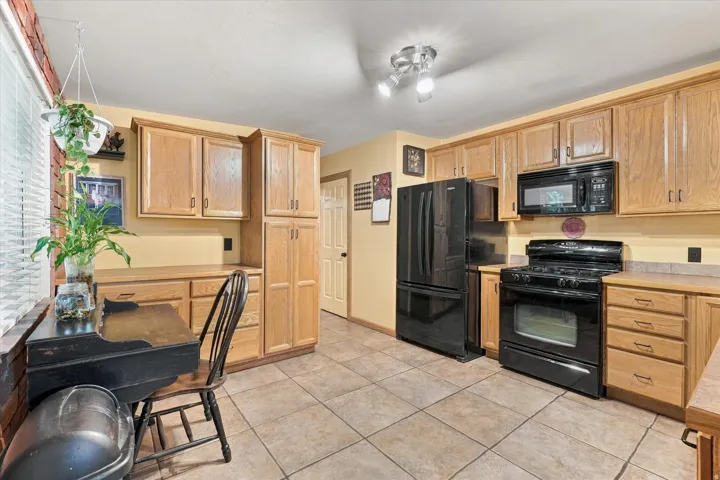 Kitchen with wood-finish cabinetry, tile flooring, and black appliances including a refrigerator, range, and microwave
