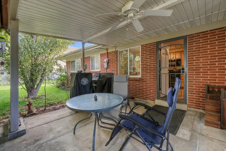 Covered patio featuring a ceiling fan, brick exterior, concrete flooring, and a security screen door
