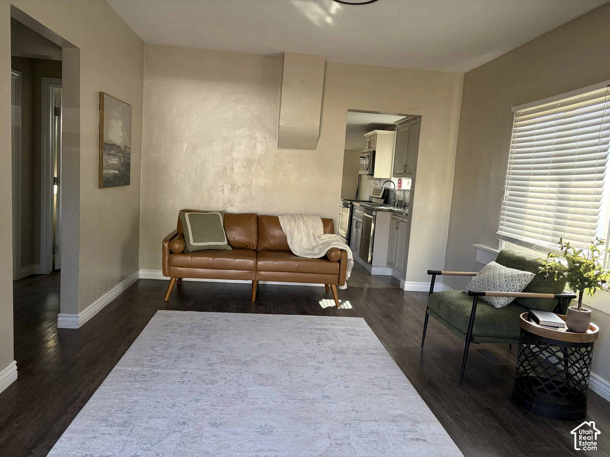 Wood-finish flooring throughout, bright window with blinds, and recessed kitchen entry