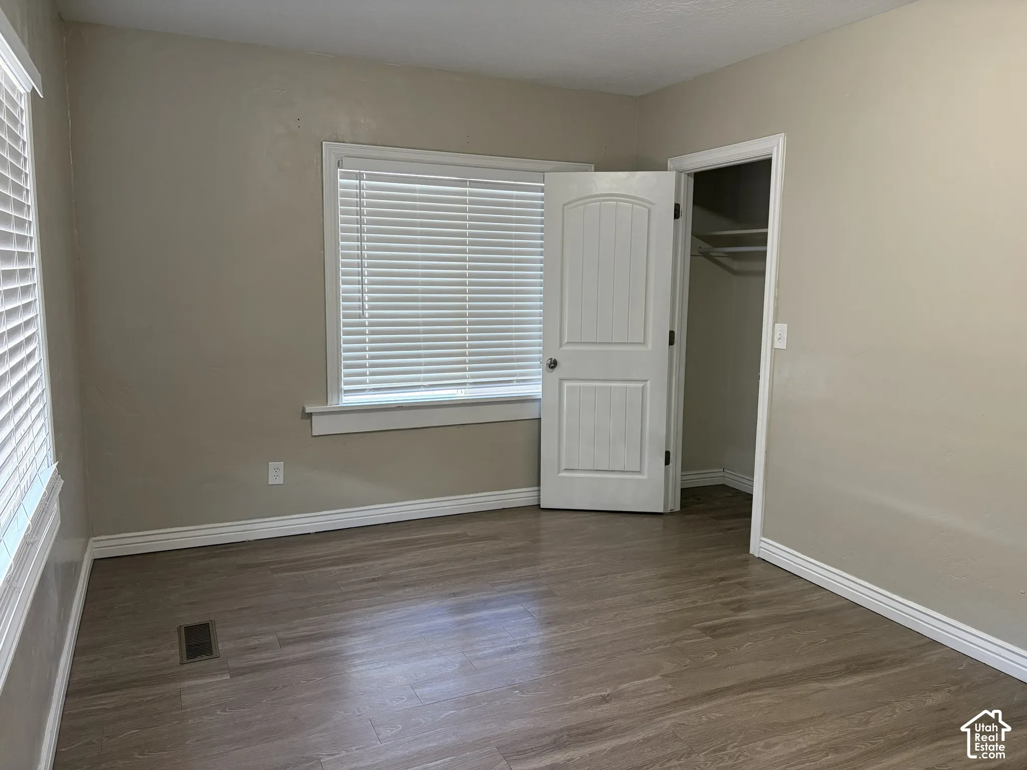 Wood-finish flooring, multiple windows with blinds, arched panel door, and built-in closet shelving