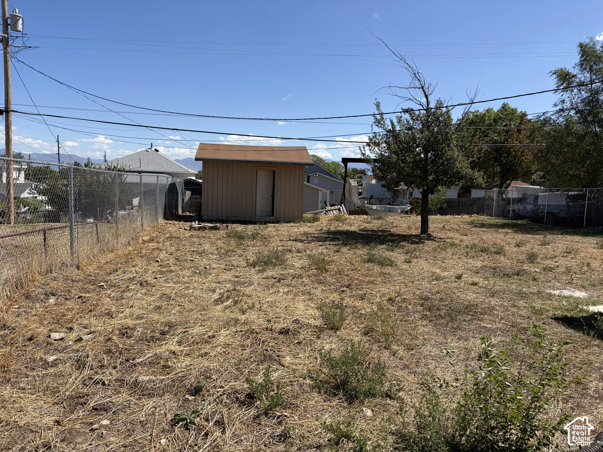 Expansive outdoor space featuring a utilitarian shed with a pitched roof, chain-link fencing, and a mature tree