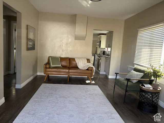 Wood-finish flooring throughout, bright window with blinds, and recessed kitchen entry