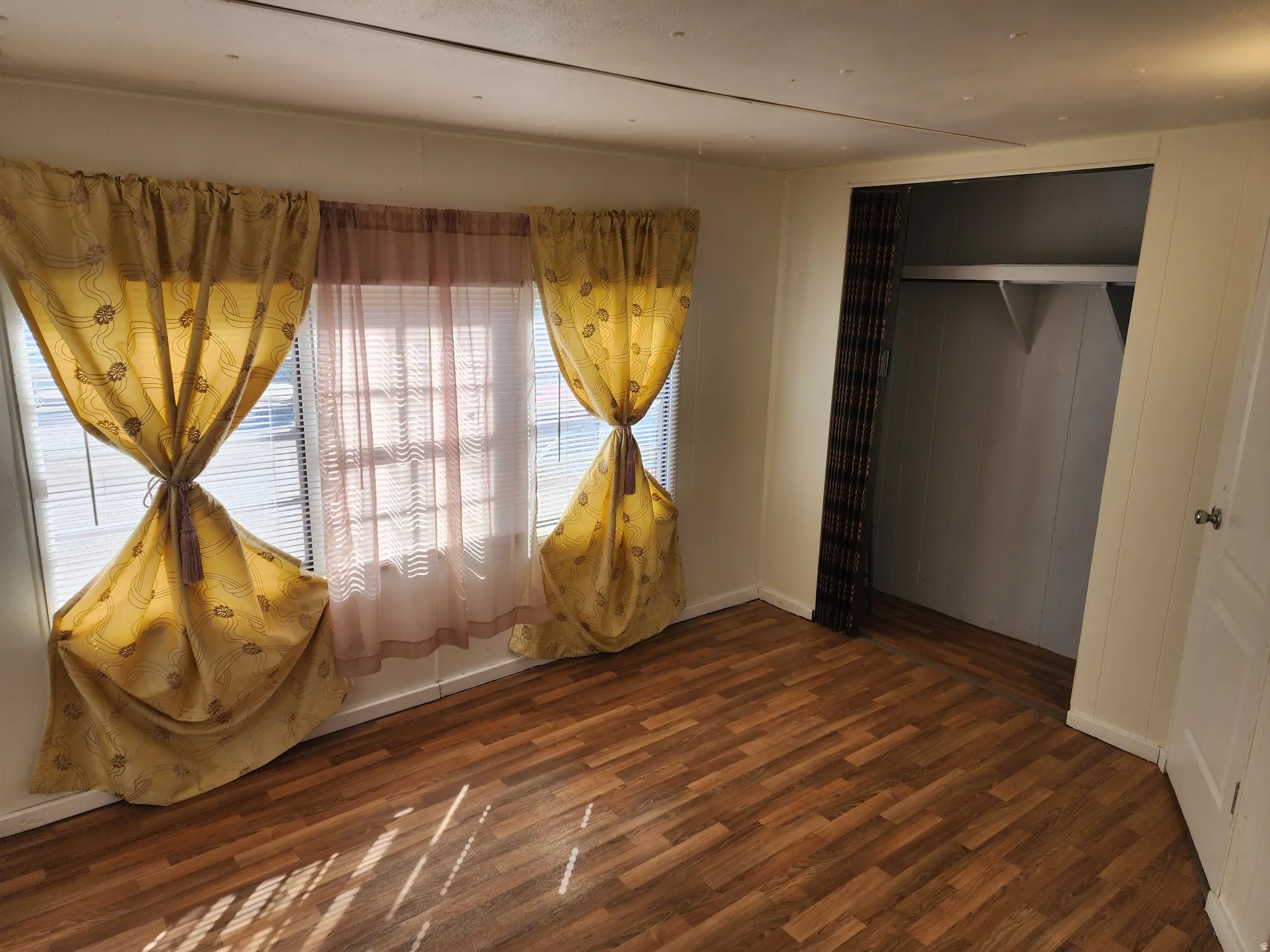 Wood-finish flooring, multiple windows with blinds, and an open closet with built-in shelving