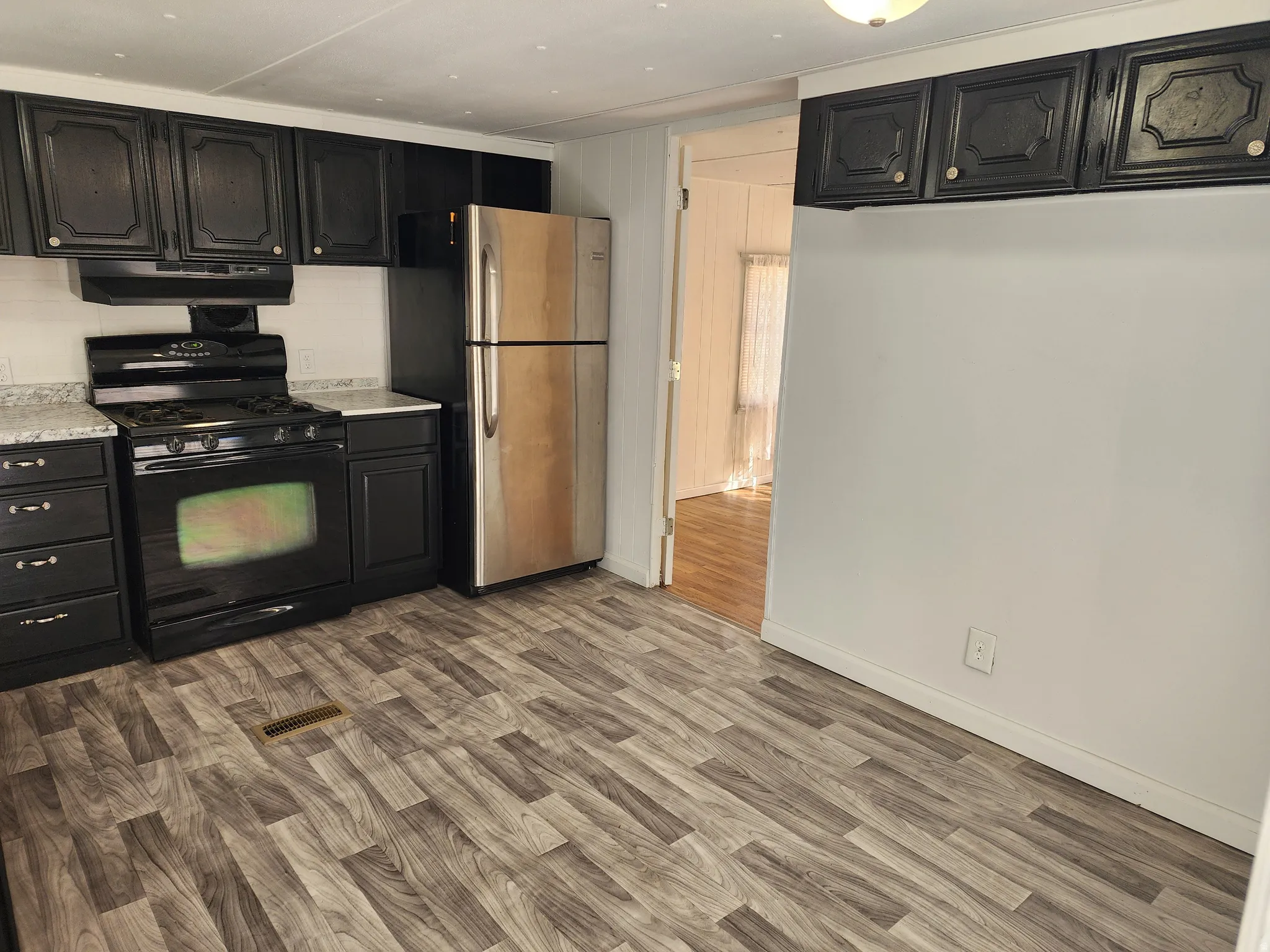 Kitchen featuring dark cabinetry, speckled countertops, stainless steel refrigerator, and wood-finish flooring