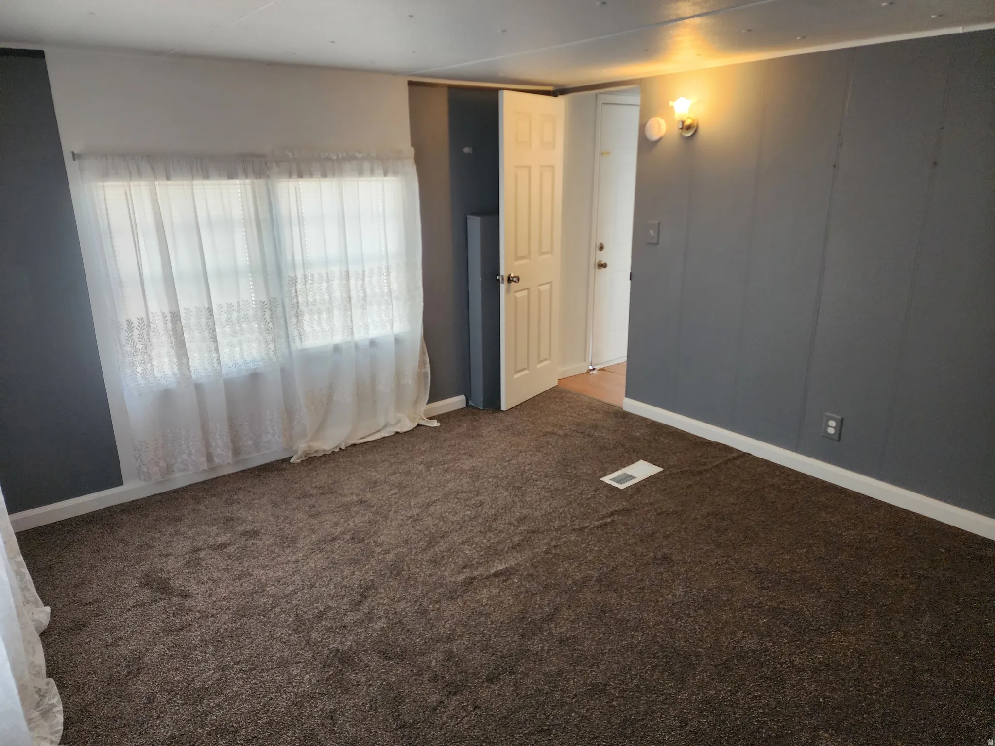 Dark gray paneled accent wall, neutral tone carpeting, white trim, and a white interior door