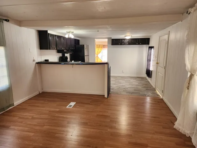 Open-concept living space with wood-finish flooring, a breakfast bar, dark cabinetry, and white paneled walls