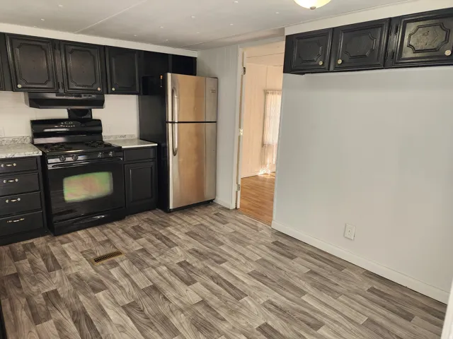Kitchen featuring dark cabinetry, speckled countertops, stainless steel refrigerator, and wood-finish flooring