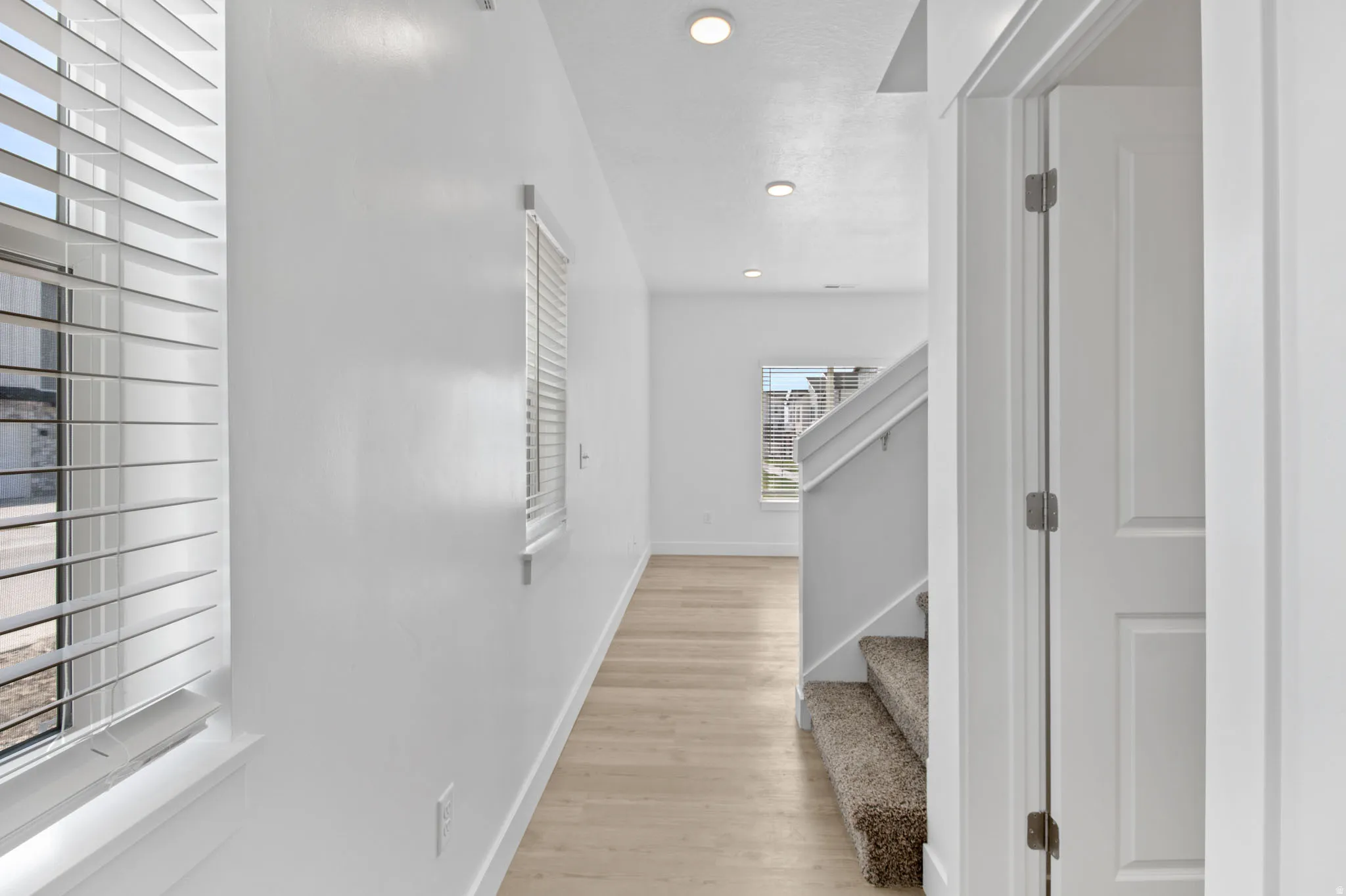 Recessed lighting, wood-finish flooring, white walls, and a staircase with carpeted treads