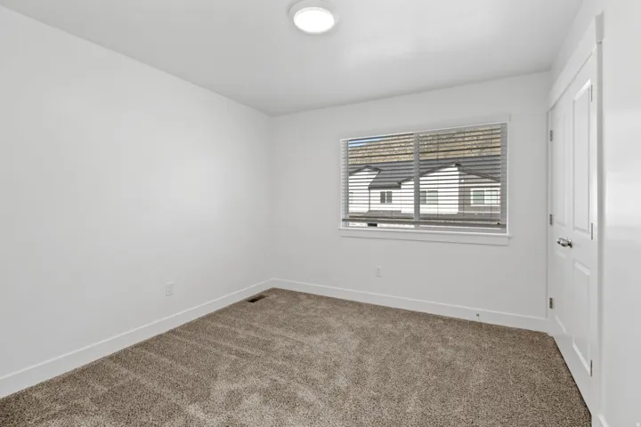 Carpeted flooring with a white trim, large window with horizontal blinds, and a white interior door with a silver handle