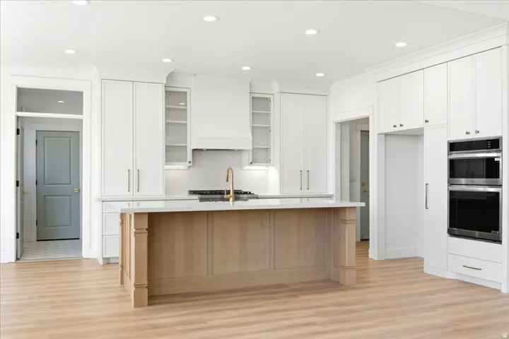 Spacious kitchen featuring light wood-finish flooring, white cabinetry with gold-tone hardware, a light wood-finish island, and built-in stainless steel appliances