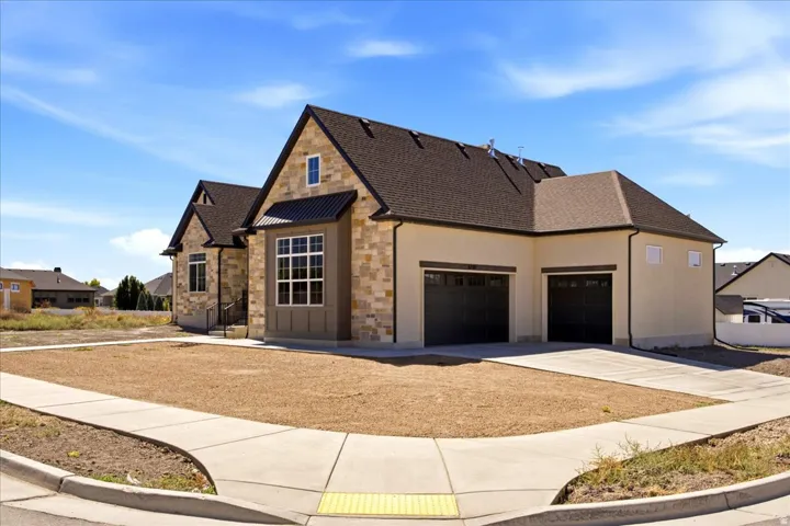 Stone veneer and stucco exterior, dark asphalt shingle roof, integrated two-car garage, multiple windows, and a concrete driveway