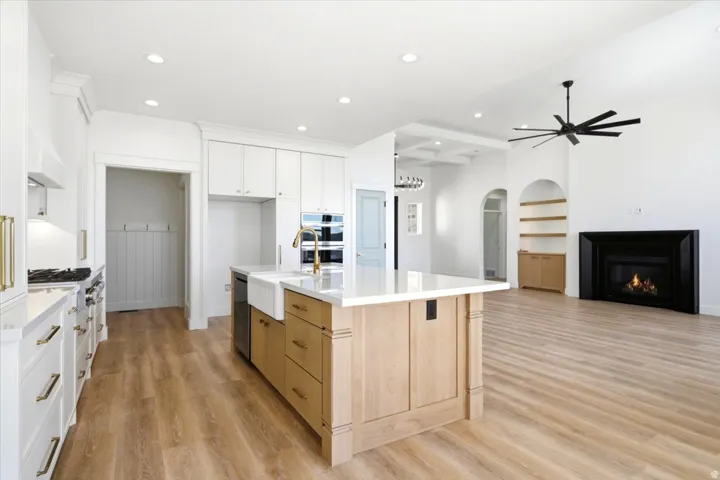 Spacious open-concept living area featuring wood-finish flooring, a central kitchen island with a farmhouse sink, stainless steel appliances, and a black fireplace with a mantel