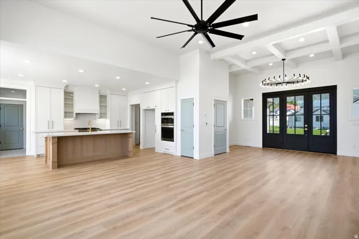 Wood-finish flooring throughout, white cabinetry with integrated appliances, kitchen island with seating, coffered ceiling, and black-framed French doors