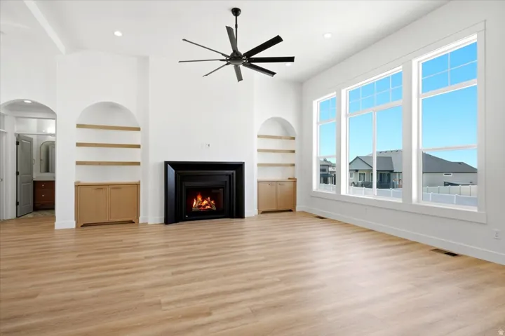 Vaulted ceiling with a contemporary ceiling fan, wood-finish flooring, a fireplace with a black surround, built-in arched shelving with lower cabinetry, and large multiple-pane windows