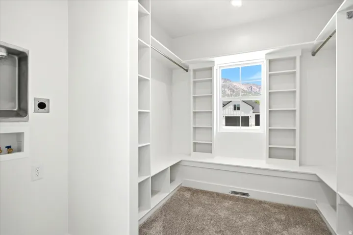 Primary walk in closet with built-in shelving, window with mountain scenery, laundry hookups, wall-mounted utility sink, and carpeting.  Don't miss the washer and dryer hooks ready to go