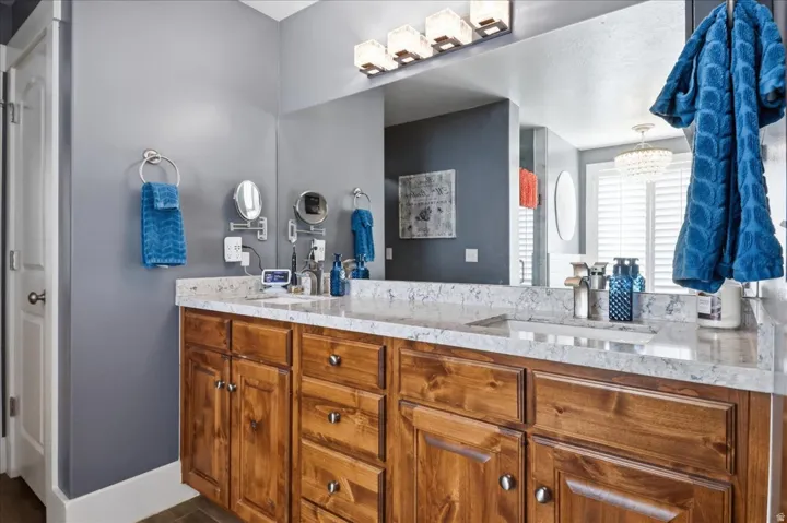 Double vanity with integrated sinks, wood-finish cabinetry, a large mirror, and a linear light fixture