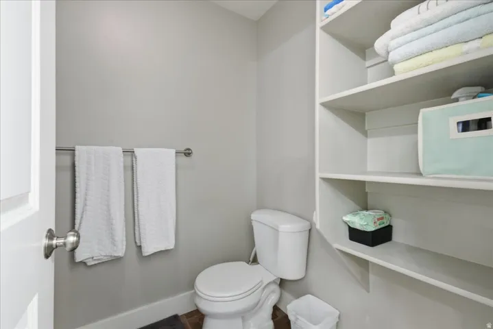 White toilet with an integrated tank, stainless steel towel bar, and built-in shelving