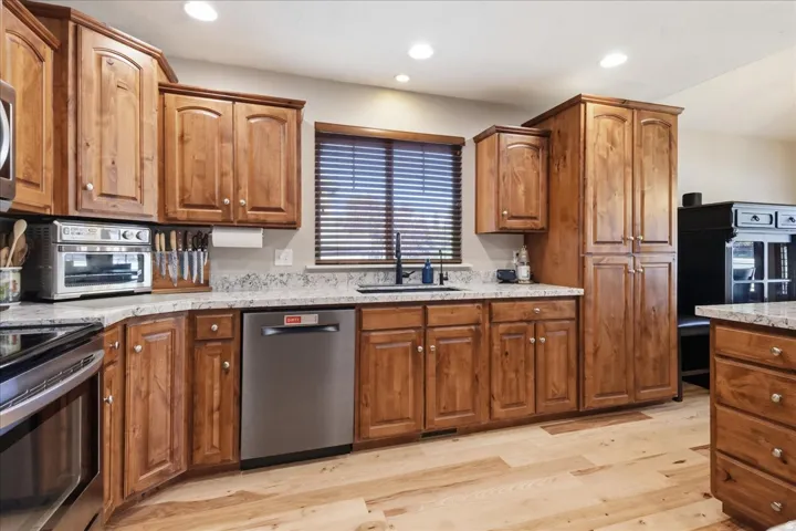 Wood-finish flooring, recessed lighting, wood cabinetry, stone countertops, and a stainless steel dishwasher