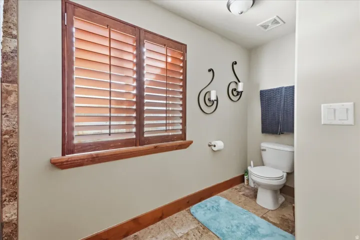 Window with wood shutters, ceramic tile flooring, built-in toilet, and ceiling-mounted light fixture