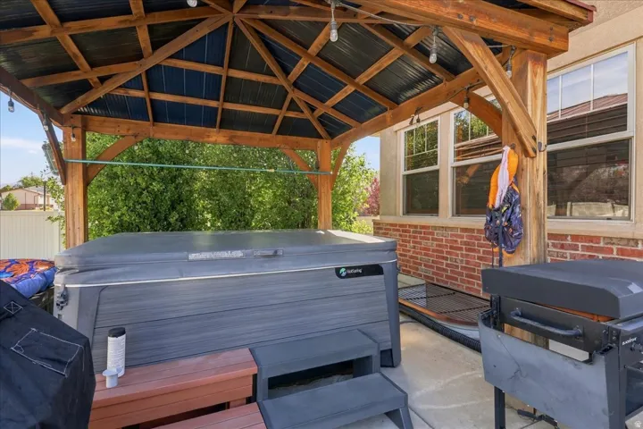Covered outdoor living space featuring a hot tub, exposed timber framing, and corrugated metal roofing