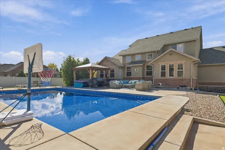 Expansive swimming pool with surrounding concrete decking, complemented by a dedicated paved patio area and an integrated wooden gazebo
