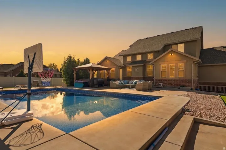 Expansive backyard with a swimming pool, concrete patio, a built-in pergola, and decorative rock landscaping