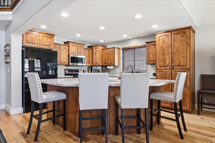 Kitchen featuring wood cabinetry, quartz countertops, stainless steel appliances, a kitchen island with seating, and wood-finish flooring