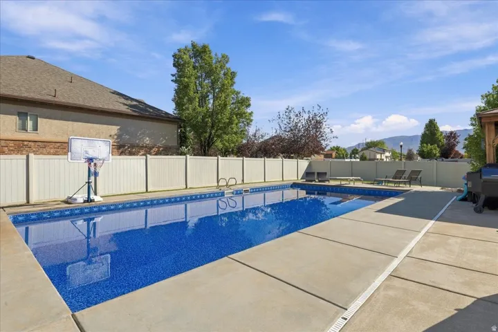 In-ground swimming pool with a concrete surround, enclosed by a privacy fence